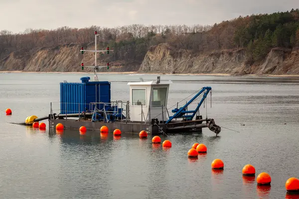 Kayalıkların yakınındaki sakin kıyı sularına demir atmış olan küçük Cutter Vakumlu Dredger çalışma botu, deniz mühendisliği veya liman bakımı için turuncu şamandıralar tarafından işaretlenmişti..