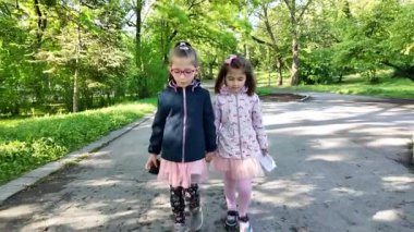 Mutlu çocuklar. Parkta yürüyen iki kız. İki küçük kız kardeş birlikte yürüyorlar, konuşuyorlar. En iyi arkadaşlar