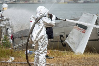  Yansıtıcı Takım Elbiseli İtfaiyeciler Çarpışma Alanındaki Uçak Yangınını Söndürüyor. İtfaiyeciler simüle edilmiş uçak kazasını su jetiyle söndürün. Acil kurtarma tatbikatı, felaket hazırlığı..