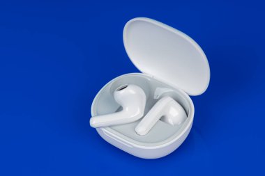 Mavi arka planda beyaz kablosuz kulaklık. Yeni kulaklıklar. Yeni teknolojiler.