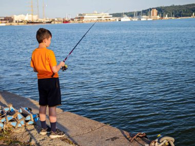 Yazın deniz kenarındaki iskelede balık tutan genç çocuk. Huzurlu çocukluk anı, açık hava eğlencesi.. 