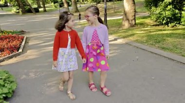 Mutlu çocuklar. Parkta yürüyen iki kız. İki küçük kız kardeş birlikte yürüyorlar, konuşuyorlar. En iyi arkadaşlar