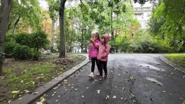 Mutlu çocuklar. Parkta yürüyen iki kız. İki küçük kız kardeş birlikte yürüyorlar, konuşuyorlar. En iyi arkadaşlar