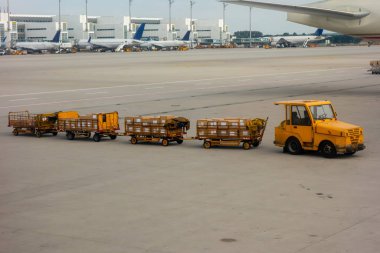 Havaalanında taşımacılık bavulları için römorklu bir traktör. Havaalanındaki yolcuların bagajlarıyla dolu karavanlar.