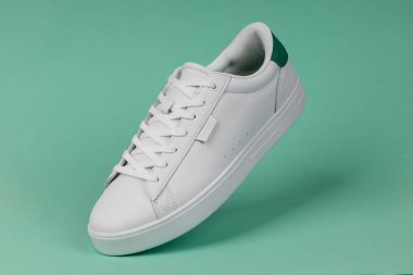 Yeşil arka planda beyaz spor ayakkabı. Günlük moda, spor giyim ve sokak kıyafetleri için modern ve şık ayakkabılar..