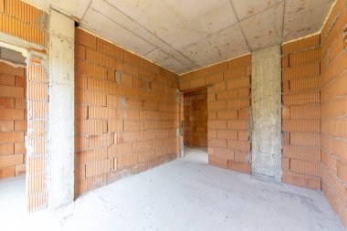 İnşaat halindeki binanın içinde bitmemiş bir oda. Tuğla kırmızı duvarlar. Yeni ev.