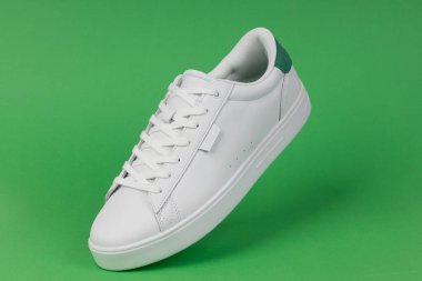 Yeşil arka planda beyaz spor ayakkabı. Günlük moda, spor giyim ve sokak kıyafetleri için modern ve şık ayakkabılar..