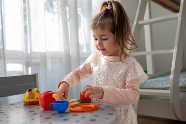 Mutlu Küçük Kız Evde Oyuncak Çay Seti ile Oynuyor. Cozy Bedroom 'da Renkli Oyuncak Seti olan Çay Partisi Oyun Saati