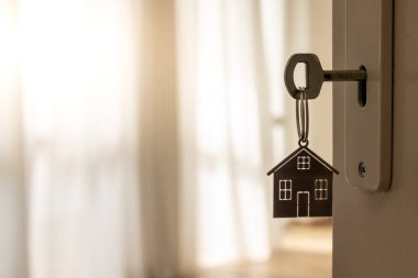 Anahtarı ve ev şeklindeki anahtarlığı olan yeni bir eve açılan kapı. İpotek, yatırım, gayrimenkul, mülk ve yeni konut kavramı