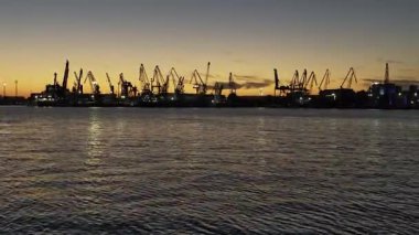 Günbatımında kargo vinçleri silueti ile sanayi limanı silueti. Ticari limanın panoramik görüntüsü, küresel ticaret, nakliyat ve lojistiği temsil ediyor.