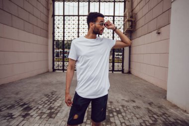 Beyaz tişörtlü Afro-Amerikan bir adam sokakta yürüyor. Model.