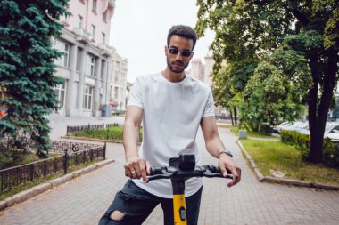 Beyaz beyaz tişörtlü ve mobiletli güneş gözlüklü Afro-Amerikan bir adam. Model.