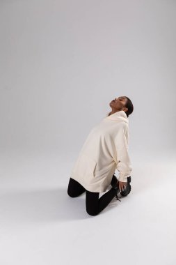 Attractive african american woman in oversized white hoodie sits on white background. Mock-up..