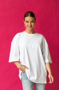 Beyaz tişörtlü, mavi pantolonlu, gri arka planda poz veren güzel sarışın kız. Yüksek kalite fotoğraf