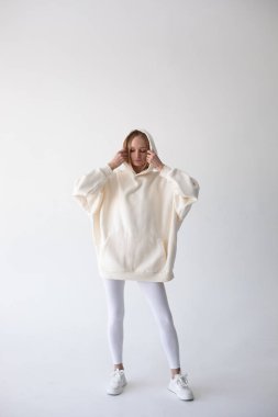 Beyaz kapüşonlu sarışın kız ve beyaz arka planda duran tayt. Yüksek kalite fotoğraf