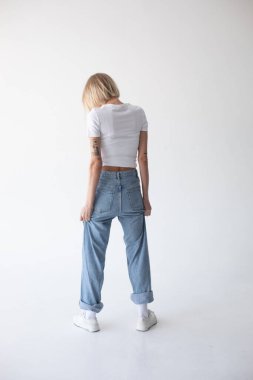 Beyaz tişörtlü, kot pantolonlu ve beyaz arka planda poz veren güzel sarışın kız. Yüksek kalite fotoğraf