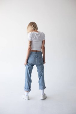 Beyaz tişörtlü, kot pantolonlu ve beyaz arka planda poz veren güzel sarışın kız. Yüksek kalite fotoğraf