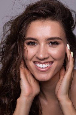 Güzel, uzun kıvırcık saçlı neşeli bir genç kadın. Yüzüne hem mutluluk hem de güven saçıyor.