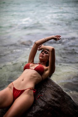 Parlak kırmızı bir bikini giymiş güzel bir kadının çarpıcı okyanusun kenarında uzandığı huzurlu ve huzurlu bir an.
