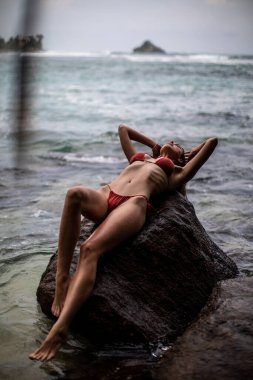 Parlak kırmızı bir bikini giymiş güzel bir kadının çarpıcı okyanusun kenarında uzandığı huzurlu ve huzurlu bir an.