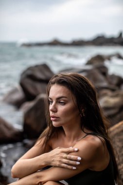 Düşünceli bir kadın sakin bir sahil şeridinde kayaların üzerinde oturmuş güzelliğin özünü bütünüyle somutlaştırıyor.