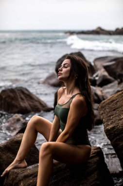 Düşünceli bir kadın sakin bir sahil şeridinde kayaların üzerinde oturmuş güzelliğin özünü bütünüyle somutlaştırıyor.