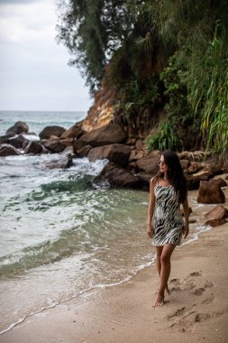 Dalgalar yavaşça ayaklarını öperken bir kadın güzel kumlu sahil boyunca huzurlu ve huzurlu bir yürüyüşün tadını çıkarıyor.