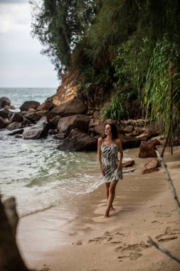 Dalgalar yavaşça ayaklarını öperken bir kadın güzel kumlu sahil boyunca huzurlu ve huzurlu bir yürüyüşün tadını çıkarıyor.