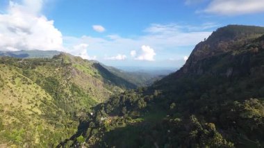 Sersemletici hava görüntülerinde parlak mavi gökyüzünün altında canlı yeşil dağlar ve dingin vadiler görülüyor.