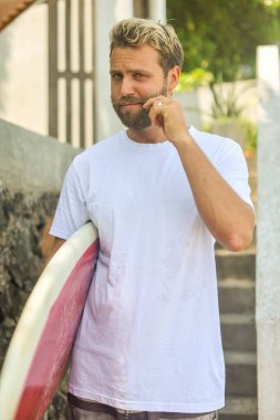 Genç bir adam sörf tahtasıyla dinlenme anının tadını çıkarıyor, canlı sörf yaşam tarzını yansıtıyor.