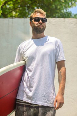 Kendinden emin genç bir adam gururla ayakta duruyor. Dalgalı ve güneşli bir tropikal plaj yerinde.