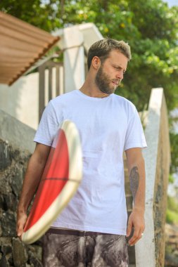 Genç bir adam sörf tahtasıyla dinlenme anının tadını çıkarıyor, canlı sörf yaşam tarzını yansıtıyor.