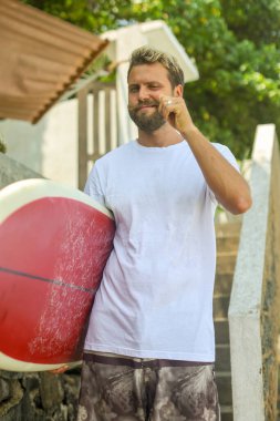 Genç bir adam sörf tahtasıyla dinlenme anının tadını çıkarıyor, canlı sörf yaşam tarzını yansıtıyor.