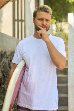 Genç bir adam sörf tahtasıyla dinlenme anının tadını çıkarıyor, canlı sörf yaşam tarzını yansıtıyor.