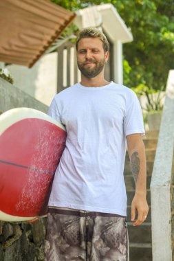 Genç bir adam sörf tahtasıyla dinlenme anının tadını çıkarıyor, canlı sörf yaşam tarzını yansıtıyor.