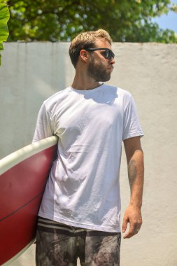 Kendinden emin genç bir adam gururla ayakta duruyor. Dalgalı ve güneşli bir tropikal plaj yerinde.