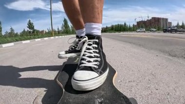 Siyah spor ayakkabılı bir kaykaycının yolda uzun bir sörf tahtası sürerken ki yavaş çekim görüntüleri. Yaz günü, güneşli hava, düşük açı görünümü hareketi, dengeyi ve şehir dışı yaşam tarzını vurguluyor..