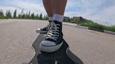 Siyah spor ayakkabılı bir kaykaycının yolda uzun bir sörf tahtası sürerken ki yavaş çekim görüntüleri. Yaz günü, güneşli hava, düşük açı görünümü hareketi, dengeyi ve şehir dışı yaşam tarzını vurguluyor..