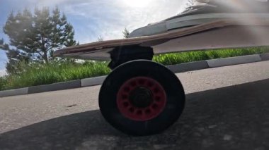 Güneşli bir gökyüzünün altında asfalt bir yolda spor ayakkabılarla uzun bir sörf tahtası süren birinin yavaş çekim görüntüleri. Düşük açıdan çekilen video, bir yaz günü boyunca hareket, yaşam tarzı ve özgürlüğü vurguluyor..