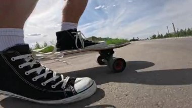 Güneşli bir gökyüzünün altında asfalt bir yolda spor ayakkabılarla uzun bir sörf tahtası süren birinin yavaş çekim görüntüleri. Düşük açıdan çekilen video, bir yaz günü boyunca hareket, yaşam tarzı ve özgürlüğü vurguluyor..