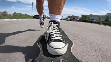 Siyah spor ayakkabılı bir kaykaycının yolda uzun bir sörf tahtası sürerken ki yavaş çekim görüntüleri. Yaz günü, güneşli hava, düşük açı görünümü hareketi, dengeyi ve şehir dışı yaşam tarzını vurguluyor..