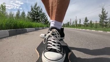 Siyah spor ayakkabılı bir kaykaycının yolda uzun bir sörf tahtası sürerken ki yavaş çekim görüntüleri. Yaz günü, güneşli hava, düşük açı görünümü hareketi, dengeyi ve şehir dışı yaşam tarzını vurguluyor..