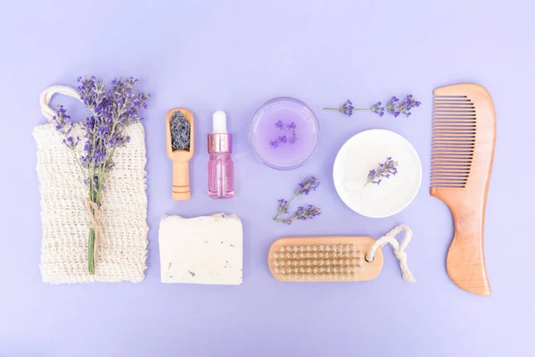 Lavender cosmetics for skin care - cosmetic oil, handmade soap, bath salt and body lotion with lavender extract over purple background. Lavender beauty products. Flat lay style