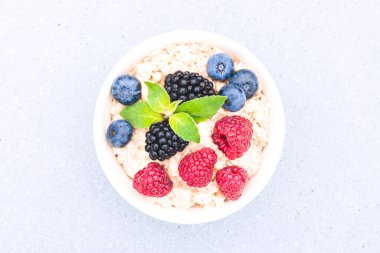Beyaz kasede yulaf lapası, ahududu, yaban mersini ve böğürtlen ile servis edilir. Sabah süper yemek lapası tarifi. Sağlıklı kahvaltı. Yukarıya bak