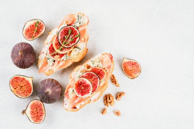 Taze kruvasan bruschetta 'ya bakın. Olgun incir, mavi peynir, prosciutto, ceviz ve otlar. Beyaz beton masa zemininde fotokopi alanı. Seçici odak