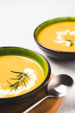 İki yeşil kase, kalın tereyağlı, bol kremalı ve biberiyeli, gri beton masa. Bir kase balkabağı ve havuç kremalı çorba. Dikey resim, en düşük biçim