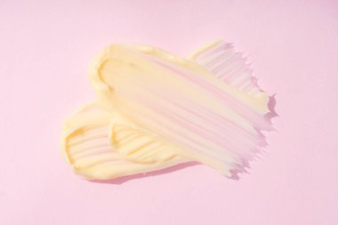 İpeksi kozmetik krem dokusu. Pembe arka planda krema ya da vücut yağı lekesi var. Cilt ürünleri