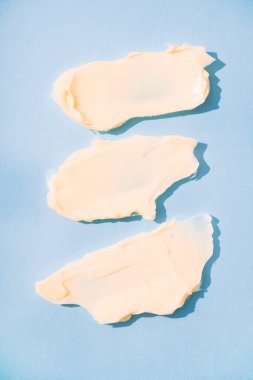 Üç krem sürme, kozmetik ürün dokusu. Pastel mavi arka planda krem lekeleri var. Cilt bakımı ve güzellik ürünü. Dikey resim