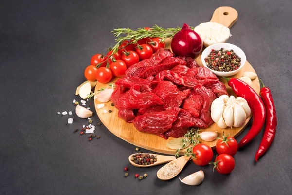 Chopped raw beef or lamb meat with seasoning and vegetables on the round wooden serving plate. Organic veal meat for cooking stew, azu or other meat main dish