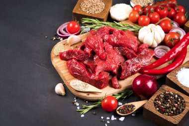 Kesilmiş çiğ et ya da kuzu eti, baharatlı, otlu ve sebzeli siyah arka planda ahşap kesim tahtasında. Pişirme güveci, azu veya diğer ana et yemekleri için organik dana eti